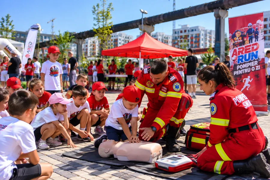 Demonstrație de prim ajutor: un copil exersează compresiile toracice pe un manechin, îndrumat de paramedici